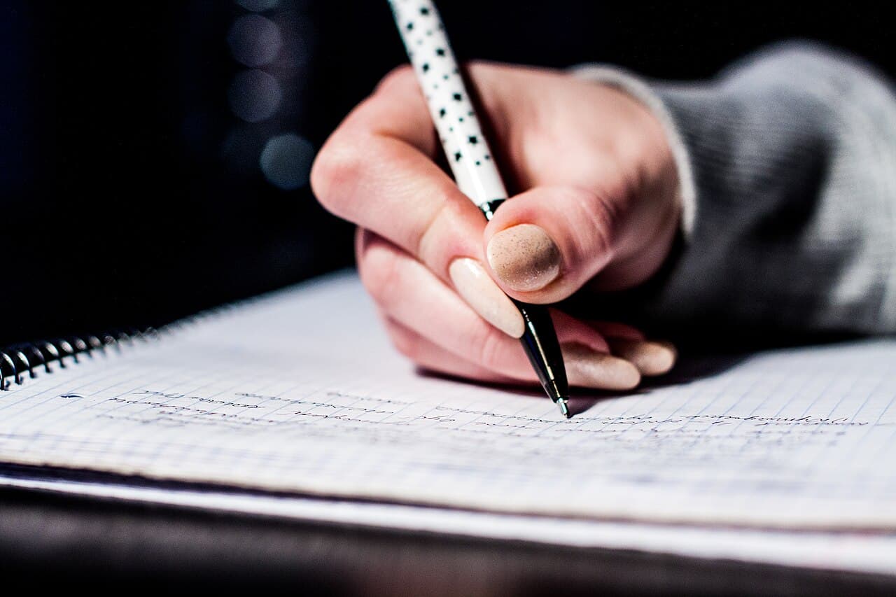 ペンでノートに書き込みながら英文法の基礎を確認する手元
